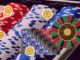 Stacks of red, white, and blue poker chips with a roulette wheel visible on the right and golden tokens floating over the chips (casino scene).